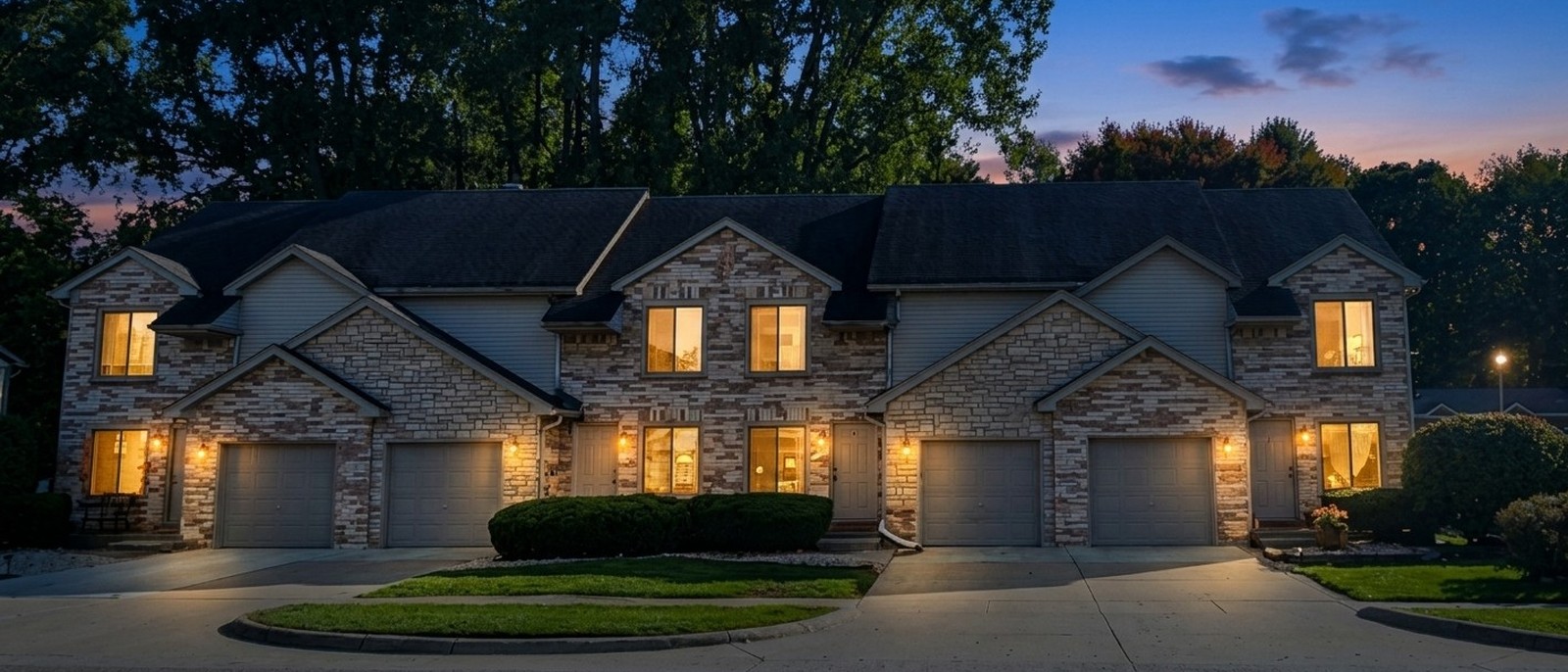Brick and stone fourplex townhouses with attached garages on Annsbury Drive, Shelby Township at twilight