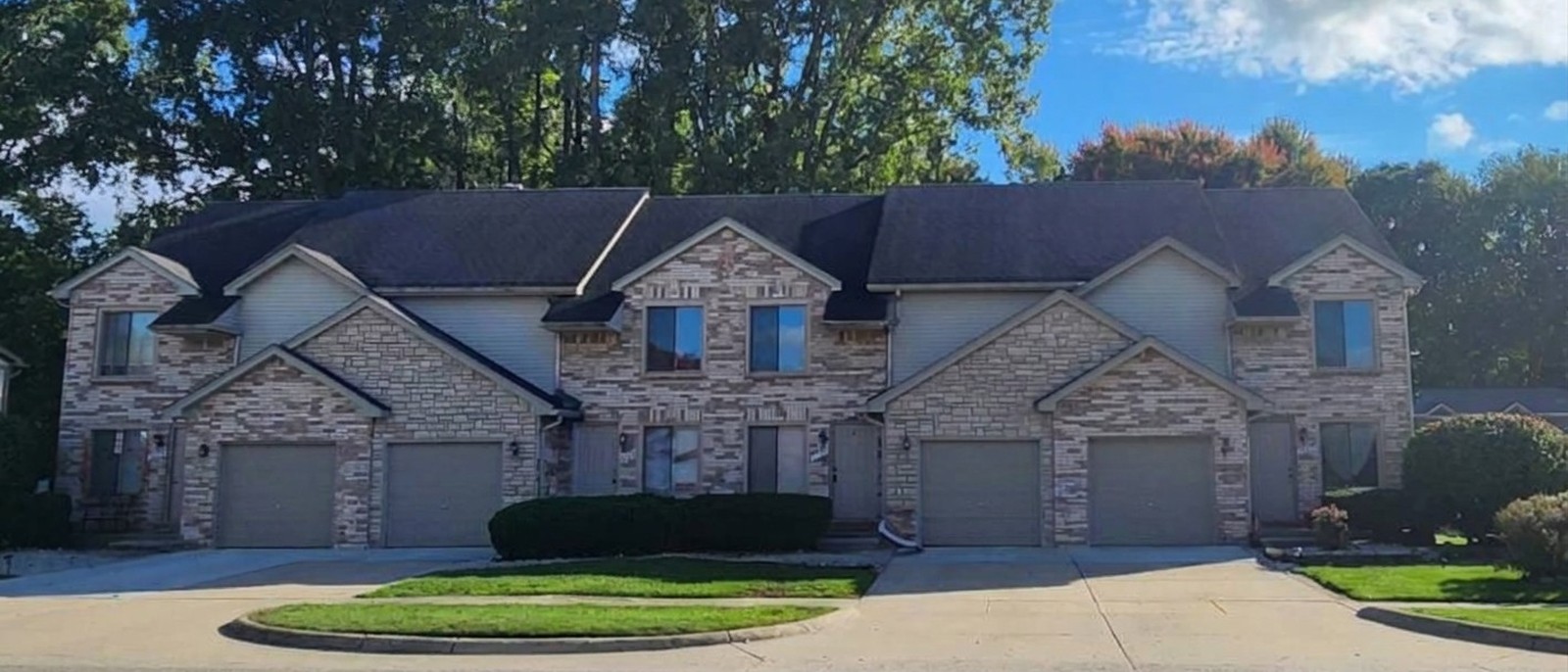 Brick and stone fourplex townhouses with attached garages on Annsbury Drive, Shelby Township by day